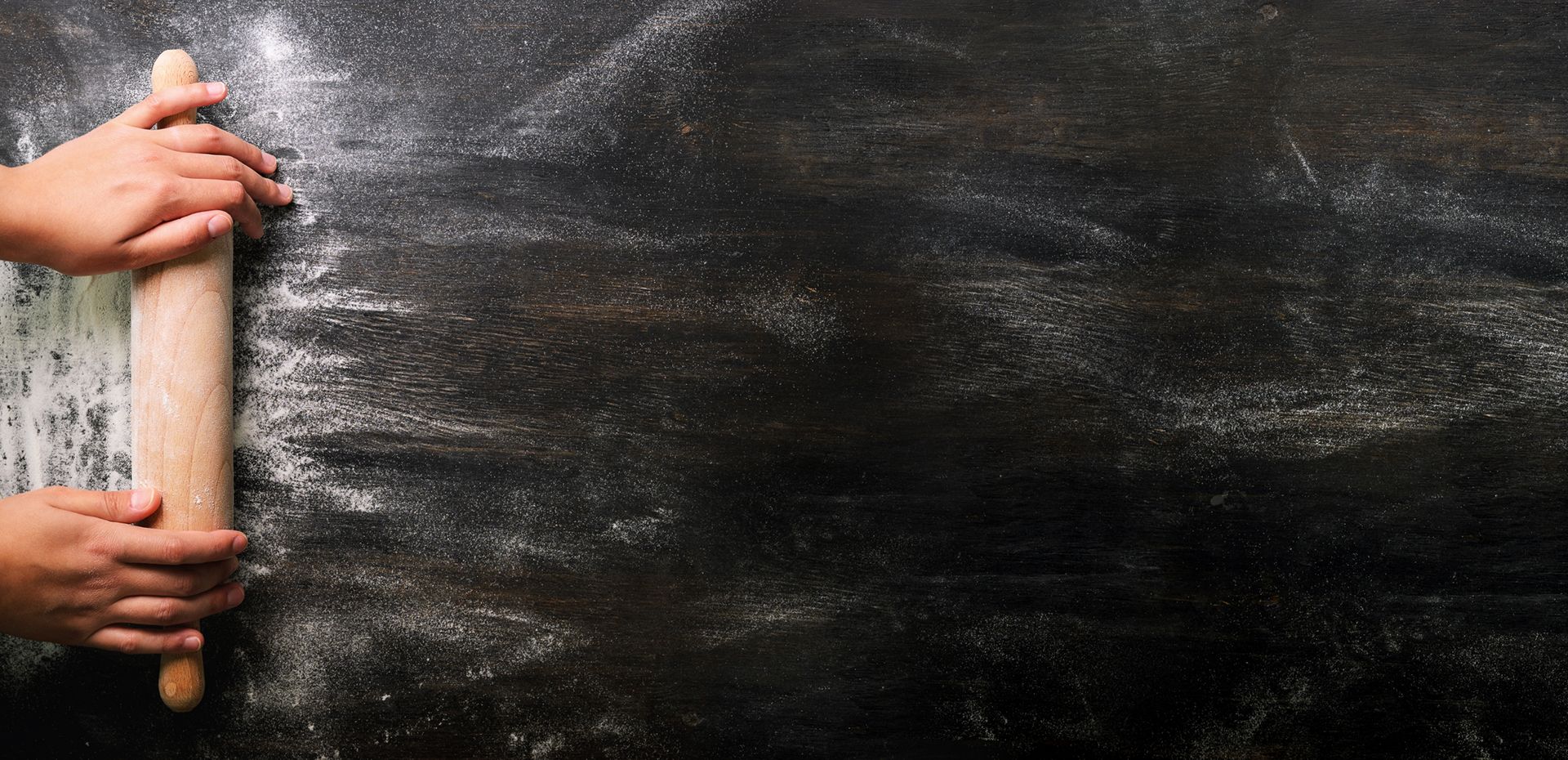 Hände mit Nudelholz auf bemehlter Arbeitsfläche beim Backen