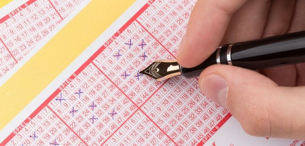 Hand mit Füller markiert Zahlen auf einem Lottoschein